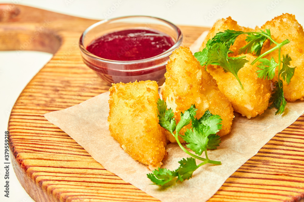 Deep fried cheese nuggets with berry sauce on a wooden board