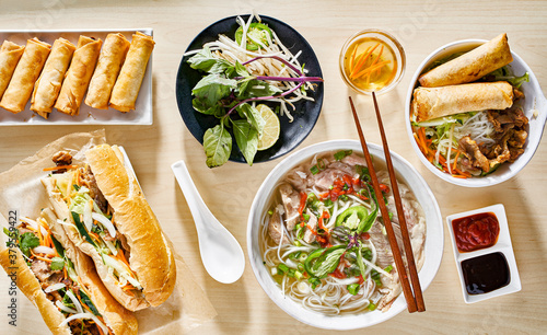 assorted vietnamese dishes with pho, bahn mi, spring rolls in top down composition on dinner table