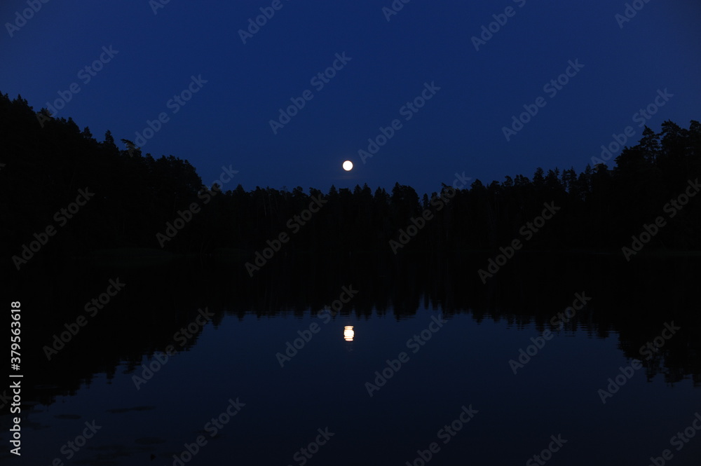 Mysterious and magic glowing full moon reflecting in a lake during night in Poland in Europe