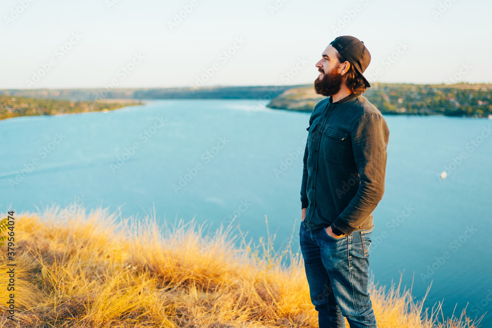 Young male standing on the field looking and smiling away near a river