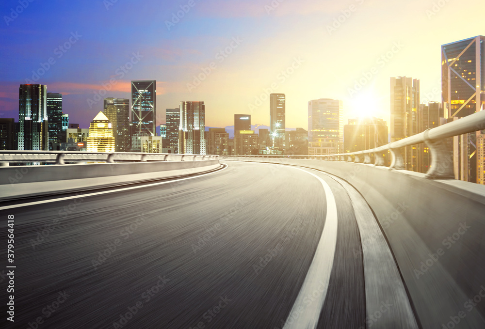 Motion blurred effect curvy overpass asphalt highway road with modern city view during sunrise.