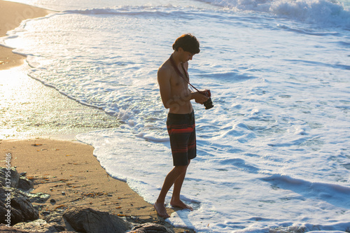 Young man in swimming trunks photographing the sea at sunset on the beach of Ikaria, Greece.