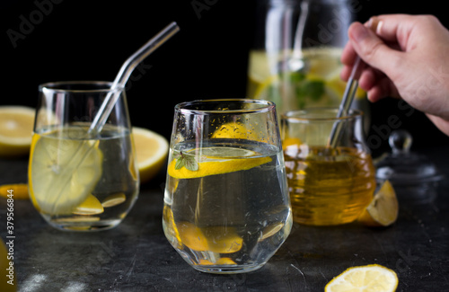 Two glasses of lemonade on a black background. Lemon slices and mint leaves float in the water and lie next to each other on the table