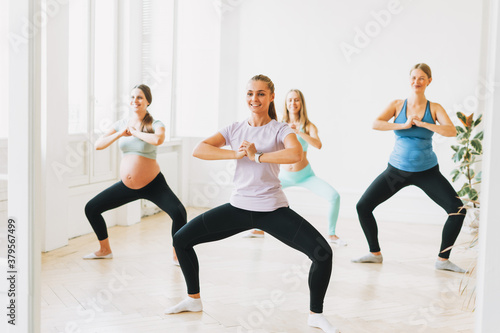 Group of pregnant women in sports uniforms with coach doing gymnastic in the bright studio