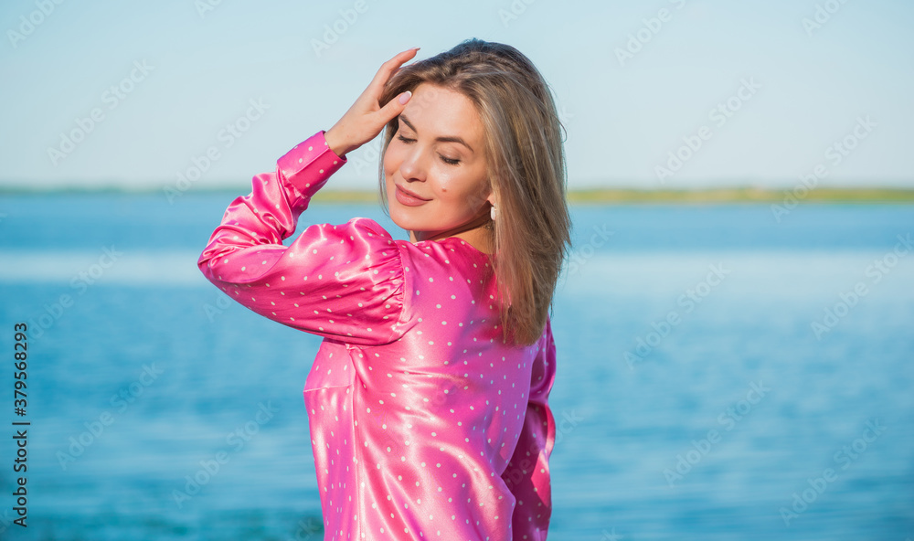 Fashionable happy woman in pink silk polka dot dress. Modern blonde hair woman at nurture in fancy romantic style Fashionable happy woman in pink silk polka dot dress. Modern blonde hair woman at nurture in fancy romantic style