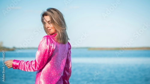 Fashionable happy woman in pink silk polka dot dress. Modern blonde hair woman at nurture in fancy romantic style 
