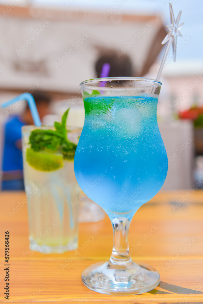 Three fresh juice drinks in tall glasses with plastic straws outside. Milkshake, blue curacao cocktail and mohito.