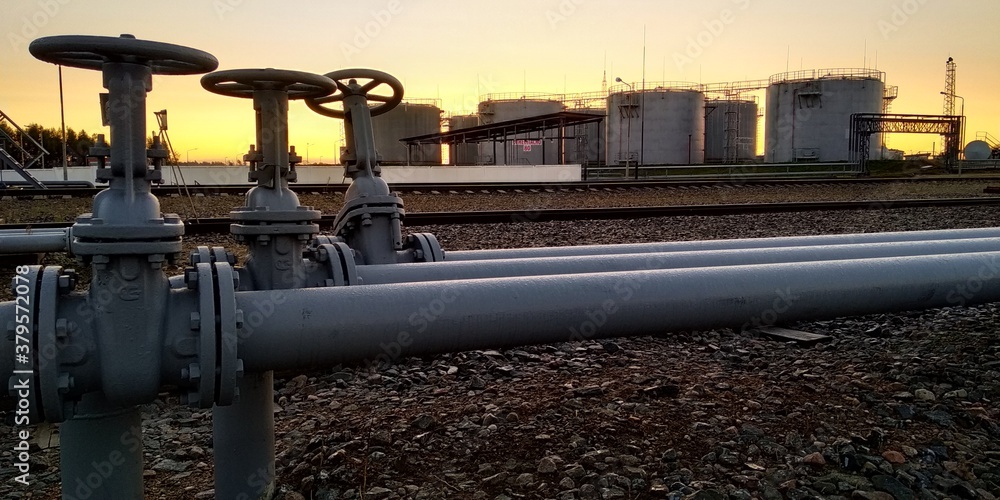 oil equipment. A valve on the pipeline, against the background of tanks for storing petroleum products.