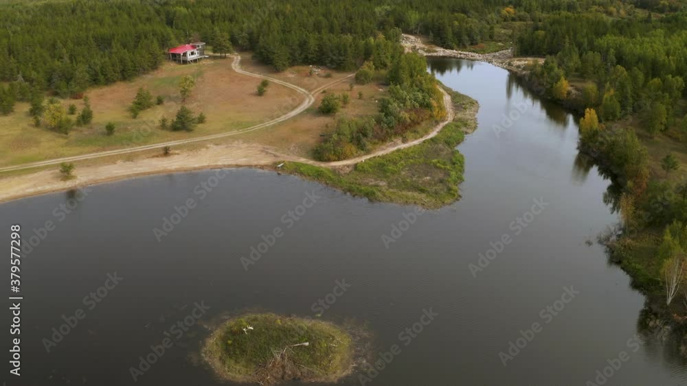 A small island in a man made lake in front of a remote cabin. Calm water held back by a dam creating a glassy smooth reflective surface. Aerial shot 4k. A small island in a man made lake in front of a remote cabin. Calm water held back by a dam creating a glassy smooth reflective surface. Aerial shot 4k.