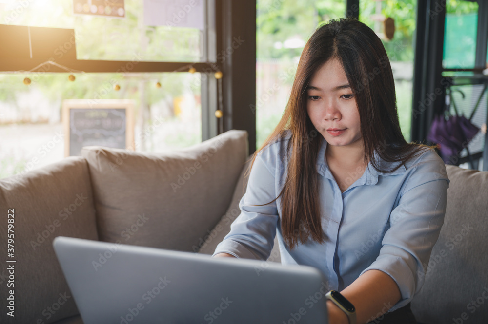A female Asian office worker of Thai descent is typing and working with notebooks in a coffee shop during the day. She was wearing a blue shirt A female Asian office worker of Thai descent is typing and working with notebooks in a coffee shop during the day. She was wearing a blue shirt
