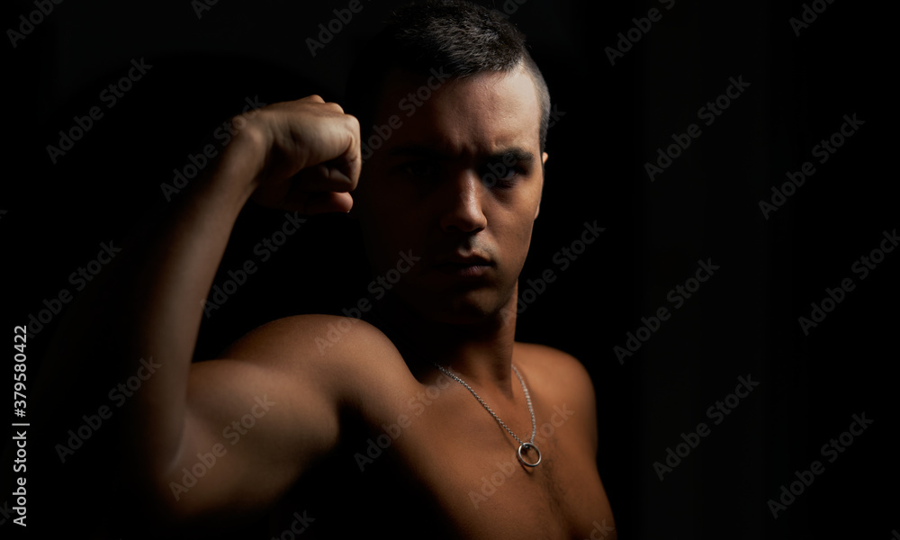 Young muscular guy looking straight ahead and showing his arm. Shirtless muscular teenage boy on black background. Young shirtless brunette on black background. Athlete and short hair with pendant Young muscular guy looking straight ahead and showing his arm. Shirtless muscular teenage boy on black background. Young shirtless brunette on black background. Athlete and short hair with pendant