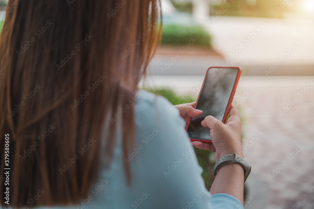 woman using a smartphone in a park, a blank smartphone screen, perspective taken from behind a person. woman using a smartphone in a park, a blank smartphone screen, perspective taken from behind a person.