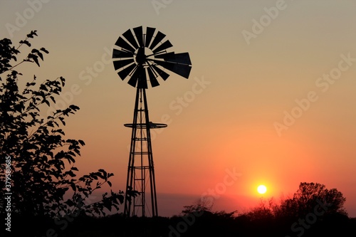windmill silhouette at sunset with tree's sky and the Sun north of Hutchinson Kansas USA out in the country.