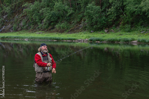 fisherman person using flyfishing rod in mountain river in waterproof cloth