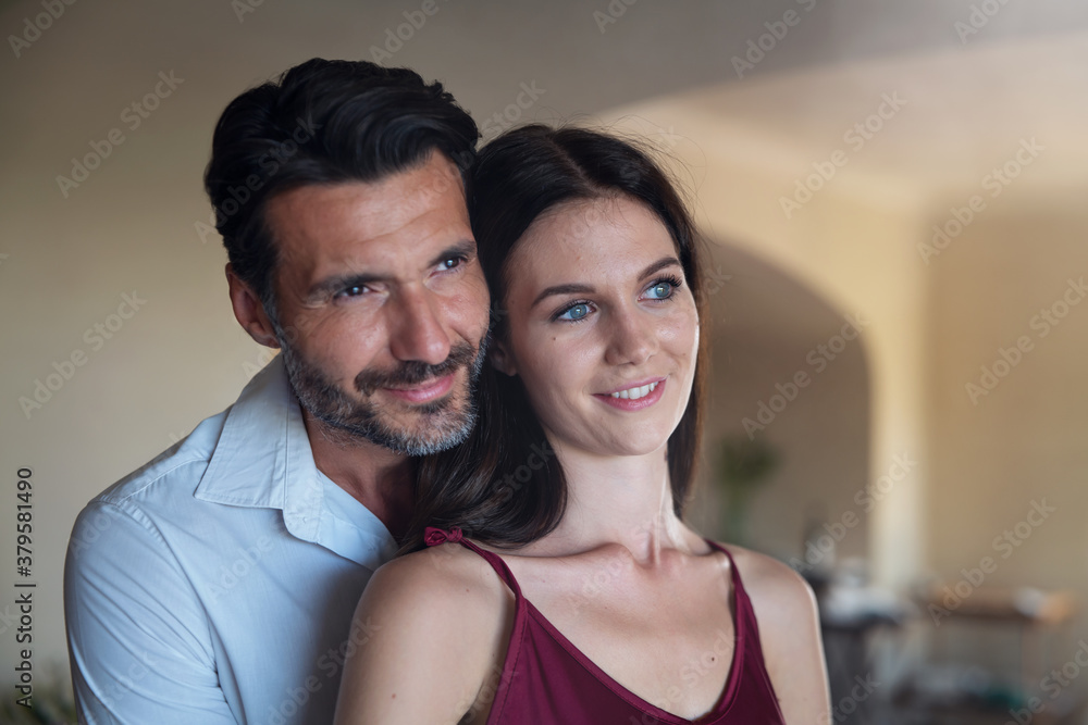 Fototapeta premium Authentic shot of happy lovely smiling married elegantly dressed couple is enjoying time together and embracing as sign of timeless love at home before going out for romantic dinner at night.