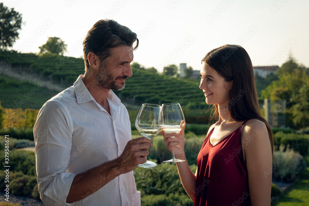 Authentic shot of happy couple in love is enjoying romantic date and cheering with white wine glasses to celebrate their anniversary and timeless love on scenic vineyards background. Authentic shot of happy couple in love is enjoying romantic date and cheering with white wine glasses to celebrate their anniversary and timeless love on scenic vineyards background.