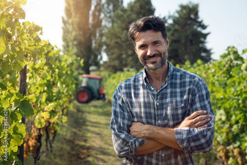 Authentic shot of happy male farmer or winemaker is smiling in camera in vineyard satisfied with results of grape harvesting for further high quality wine production. photo