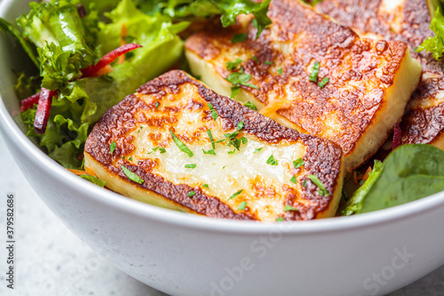 Green salad with grilled halloumi cheese in white bowl. Cypriot or Greek food concept. photo