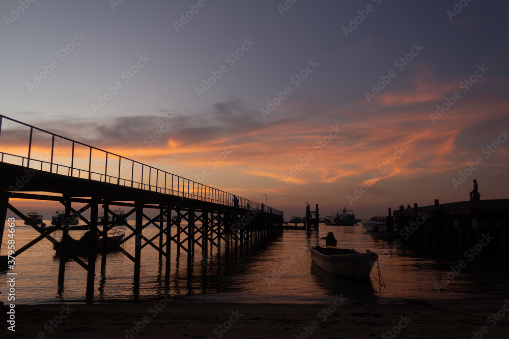 Obraz premium Atardecer anaranjado en puerto con barcos y puente
