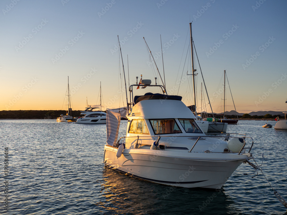 Beach in the Formentera island with yacht in the water anchored during sunset. Calm ocean water in the coast