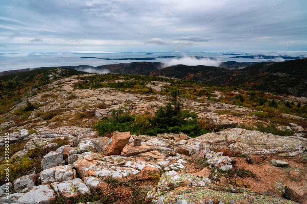 Acadia national park turns colors with the season in October and shines with a glow as the sun breaks the horizon on a cloudy early morning in Bar Harbor Maine at top of Cadillac Mountain after hiking