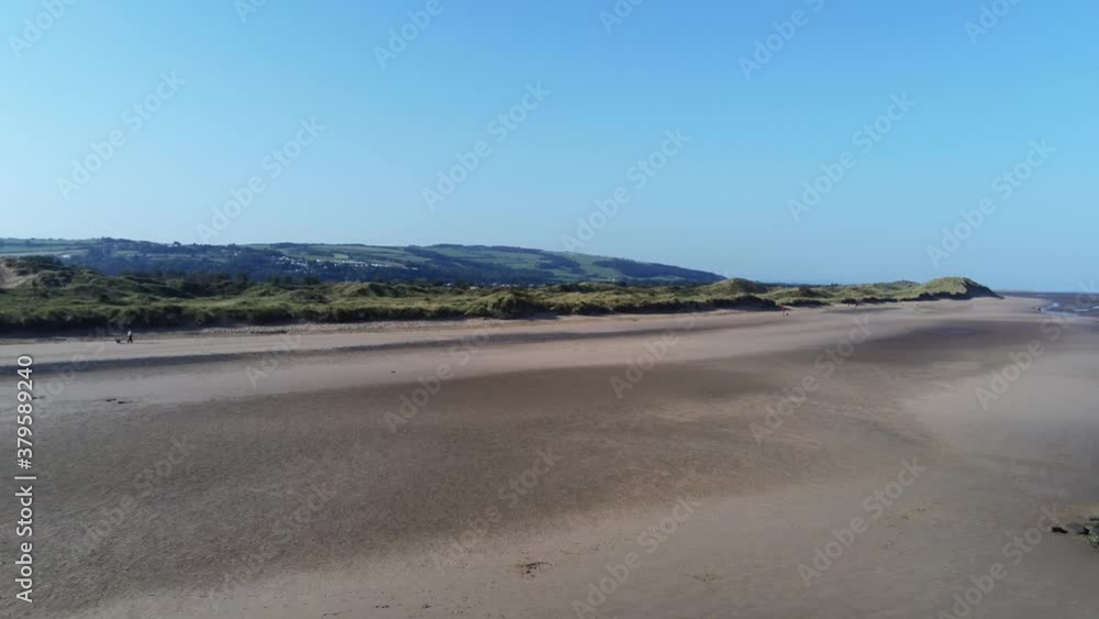 Blue sky golden North Wales low tide sandy shoreline aerial view pan right across coastal landscape Blue sky golden North Wales low tide sandy shoreline aerial view pan right across coastal landscape