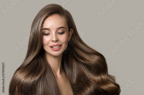 portrait of beautiful smiling brunette woman with wavy hair. Woman with hairstyle and makeup on gray background
