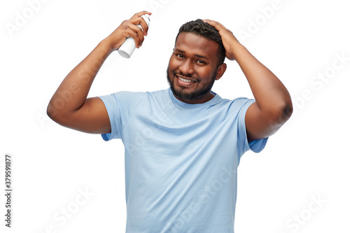grooming, hairstyling and people concept - smiling young african american man applying hairspray to his hair spray over white background