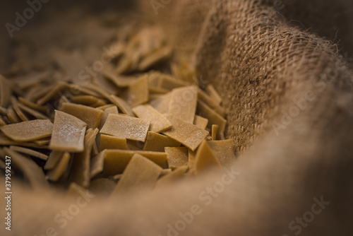 Fototapeta Naklejka Na Ścianę i Meble -  Small flat squares of homemade pasta in the dry state. An irregular shape created so as not to waste even the smallest scrap of dough.