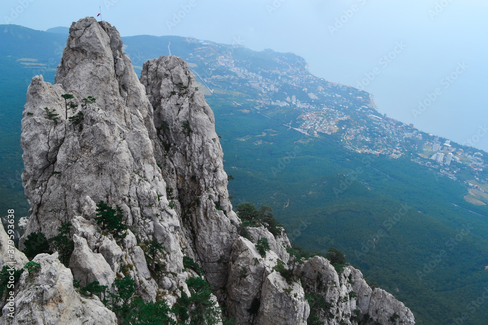large steep sharp stone rock Ai-petri with green trees stands on a cliff against the background of Black sea coastline in Crimea, the city below large steep sharp stone rock Ai-petri with green trees stands on a cliff against the background of Black sea coastline in Crimea, the city below