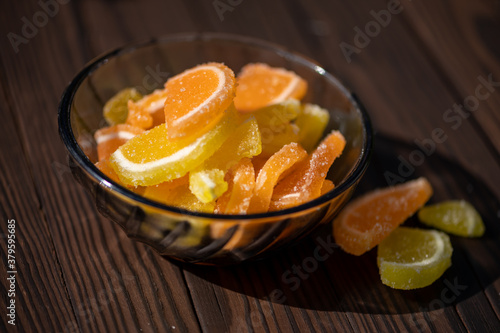 Marmalade lemon slices in a glass vase on a wooden table in the sunlight, close-up, selective focus.