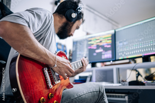 Young musician playing electric guitar with headphones at home studio. Music and professional musicians concept