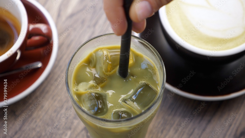 Top view of hand stirring matcha ice green tea with plastic straw. Vegan refreshing beverages Top view of hand stirring matcha ice green tea with plastic straw. Vegan refreshing beverages