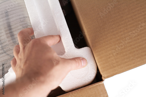 Packing goods in cardboard box with styrofoam material for safe transportation of cargo. Isolated on white background. Man's hands are packing the goods. photo