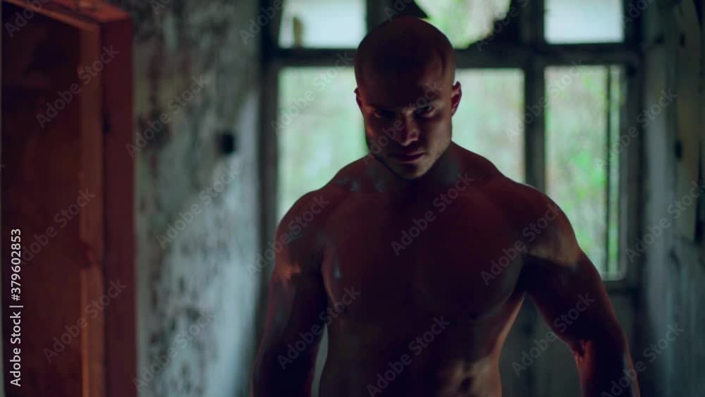 Athletic man with a naked torso doing biceps curls. Stands in smoke in a ruined building Athletic man with a naked torso doing biceps curls. Stands in smoke in a ruined building