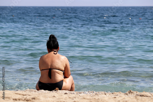 Fototapeta Naklejka Na Ścianę i Meble -  Fat woman sitting on a beach on sea waves background. Overweight and obesity concept