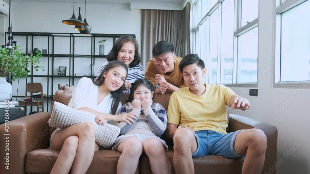 Excited big asian multi age family cheering in front of tv. big happy family watching sport match on tv movies feeling excited and thrilled on sofa in living room home interior background Excited big asian multi age family cheering in front of tv. big happy family watching sport match on tv movies feeling excited and thrilled on sofa in living room home interior background