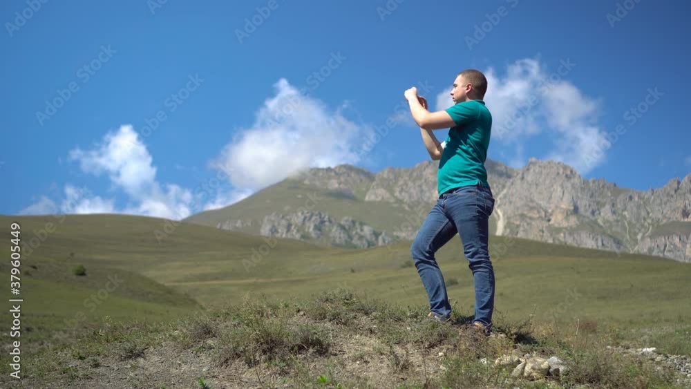A young man stands in the mountains and takes pictures on the phone. A man travels in the Caucasian mountains. A young man stands in the mountains and takes pictures on the phone. A man travels in the Caucasian mountains.