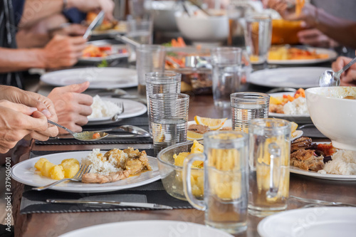 Close up of group of people gathering for eating food together and enjoying the party and communicate with family and friends at table on holiday. People passing dishes to each other