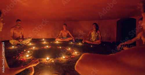 Group of people inside Mayan Temazcal- traditional steam sauna bath of Mesoamerican cultures. Diverse multiethnic people sitting around candle lights in circle in darkness and meditating