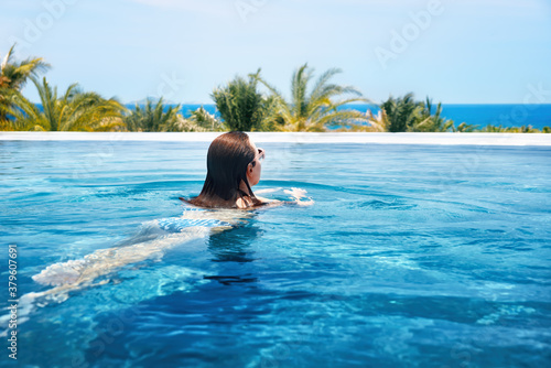 Beautiful woman swims in luxury outdoor pool the background of ocean.