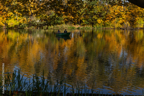 beautiful autumn landscape yellow trees reflected in the water of the lake fishermen catching fish © Tania