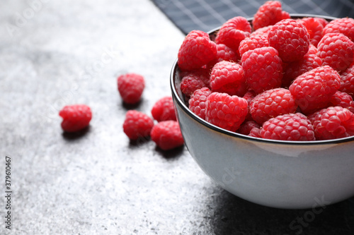 Delicious fresh ripe raspberries in bowl on grey table, closeup. Space for text