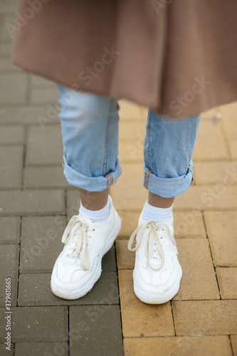 Women's shoes for lifestyle. Female feet in white sneakers and jeans