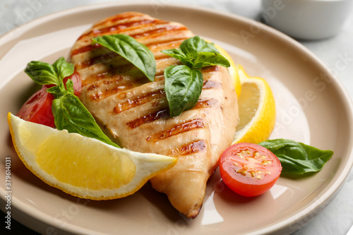 Tasty grilled chicken fillet with green basil, lemon slices and tomato on plate, closeup
