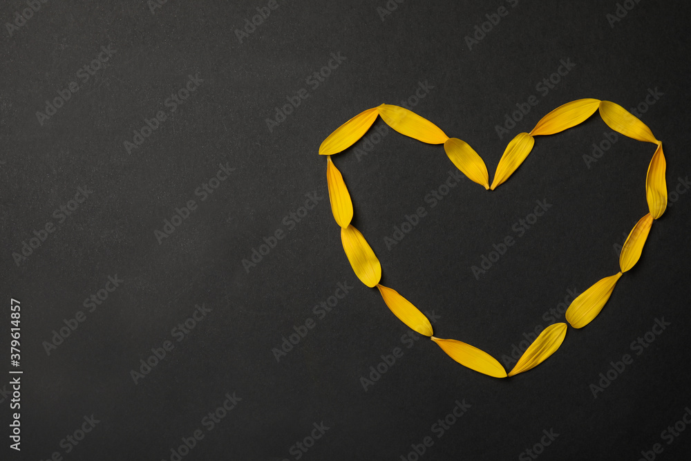 Heart shaped frame made with yellow sunflower petals on black background, flat lay. Space for text