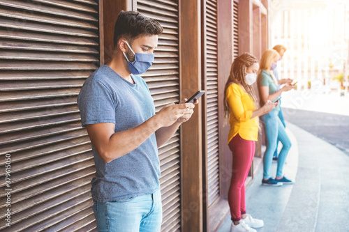 Young people wearing face safety masks using smart mobile phones while keeping social distance during coronavirus time - Technology and covid-19 spread prevention concept - Focus on man hands