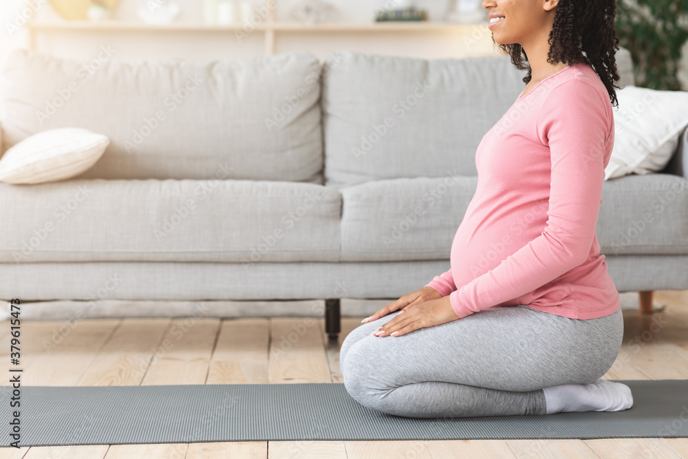 Pregnant black woman sitting on mat, getting ready before exercising