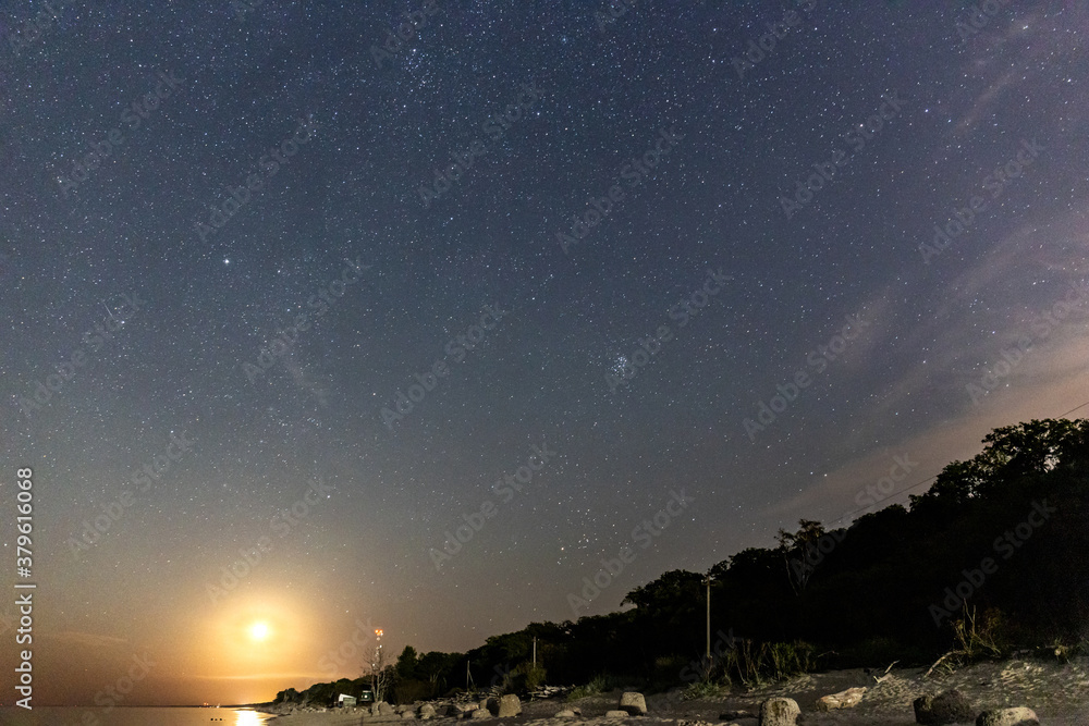 night starry sky with rising moon over sea beach