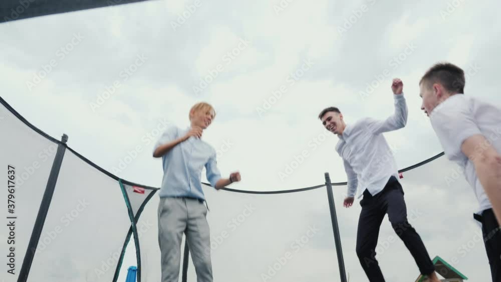 Three high school graduates jump on a trampoline, having fun on the day of their graduation Three high school graduates jump on a trampoline, having fun on the day of their graduation